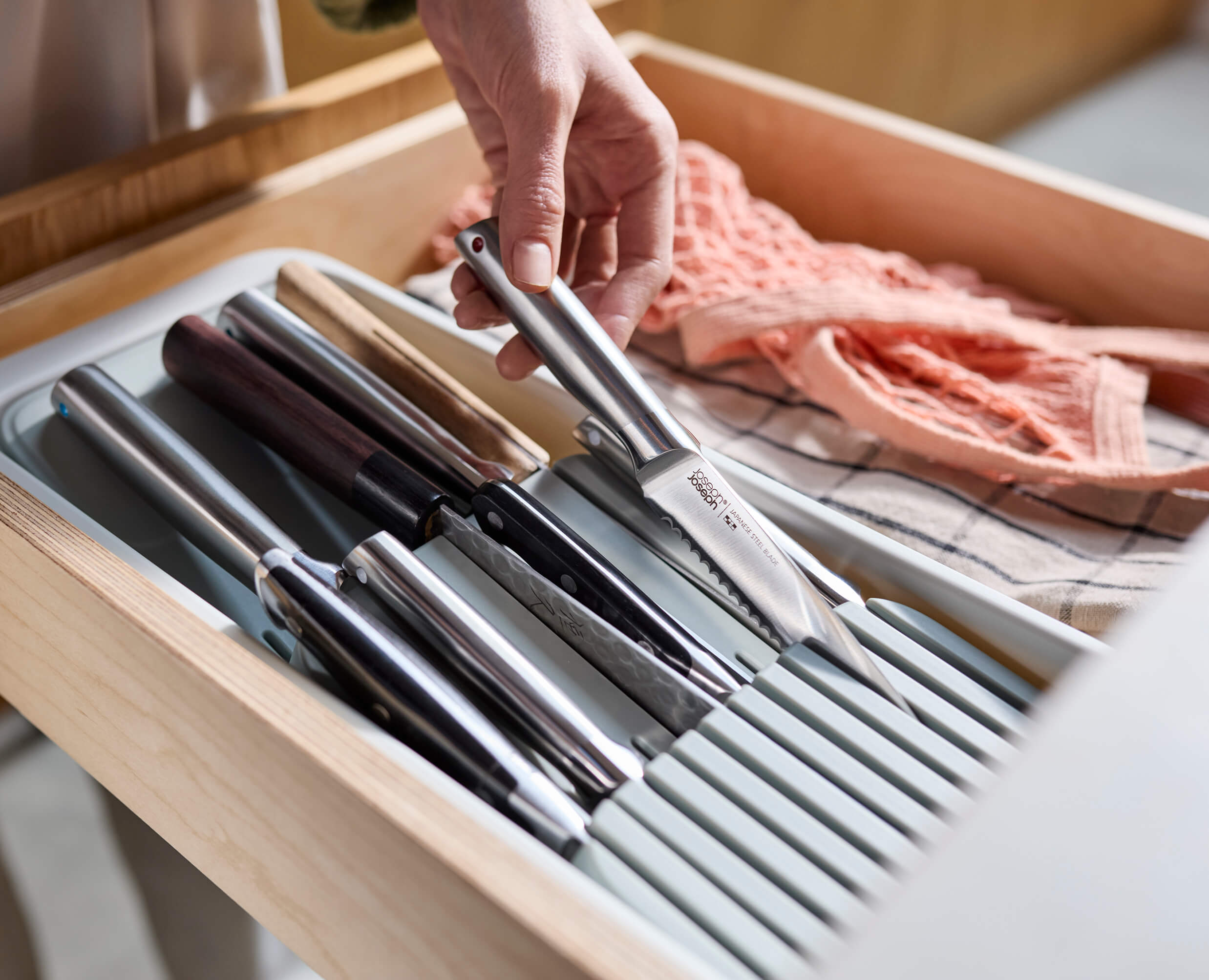 Joseph Joseph 8500013. Stone knife organizer in a drawer with example knives and a hand removing one.